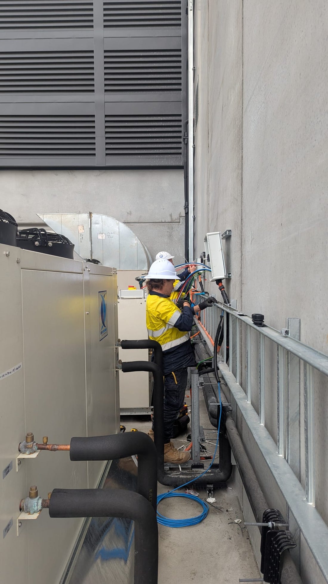 Technicians making electrical connections to chiller plant on a rooftop access walkway